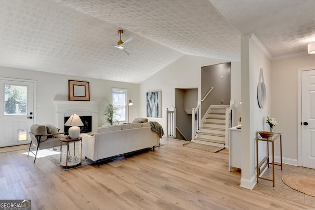 living room with a fireplace, lofted ceiling, light wood-style flooring, a textured ceiling, and stairs