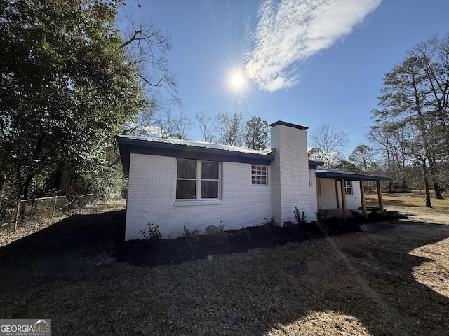 view of home's exterior with a chimney, metal roof, and brick siding