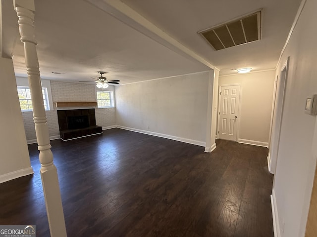 unfurnished living room with visible vents, dark wood-style floors, brick wall, ceiling fan, and a fireplace