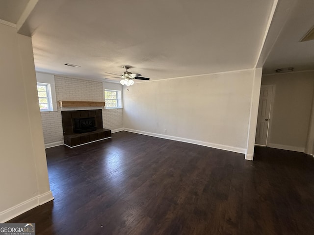 unfurnished living room featuring a healthy amount of sunlight, brick wall, visible vents, and dark wood finished floors