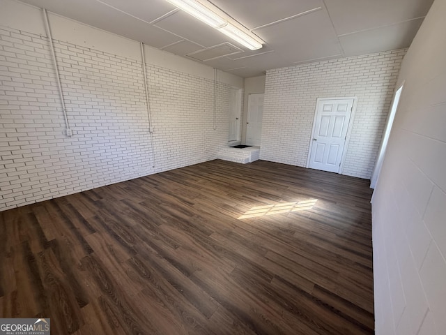 unfurnished room featuring brick wall and dark wood-type flooring