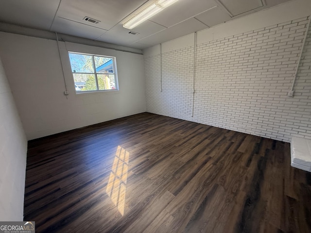 unfurnished room with visible vents, dark wood finished floors, and brick wall