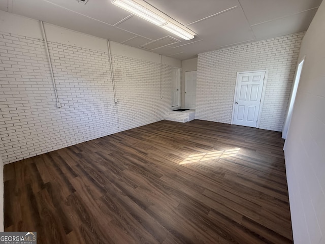 empty room with dark wood finished floors and brick wall