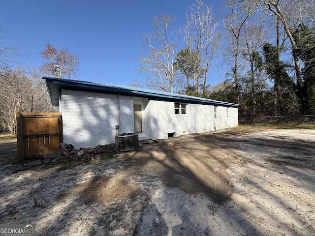 exterior space featuring brick siding, central AC unit, crawl space, fence, and metal roof