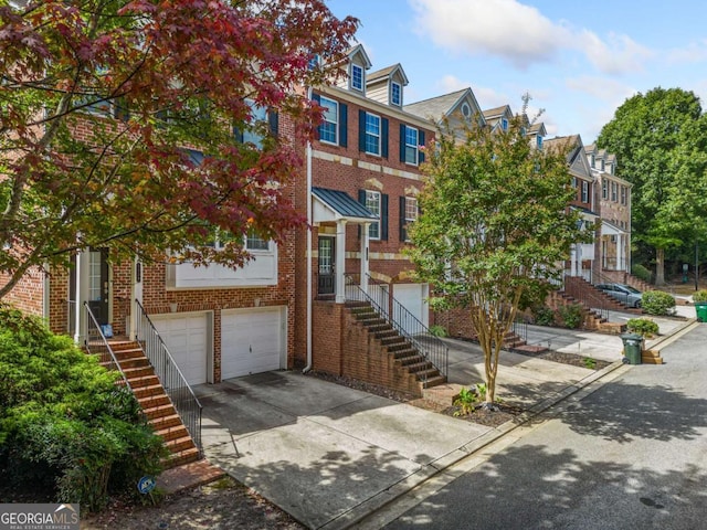 view of property featuring a garage, concrete driveway, brick siding, and stairs