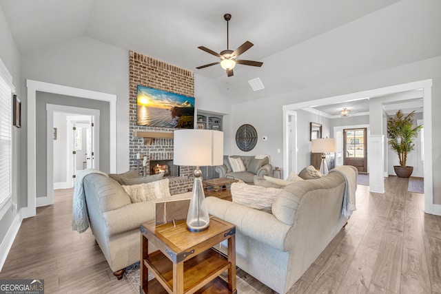 living area with lofted ceiling, a brick fireplace, baseboards, and wood finished floors