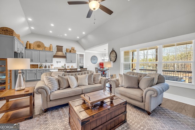 living room featuring lofted ceiling, recessed lighting, ceiling fan with notable chandelier, wood finished floors, and baseboards