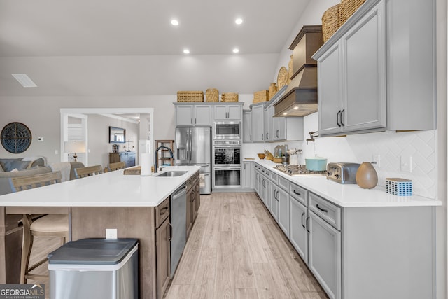 kitchen featuring a breakfast bar area, a sink, light countertops, appliances with stainless steel finishes, and an island with sink