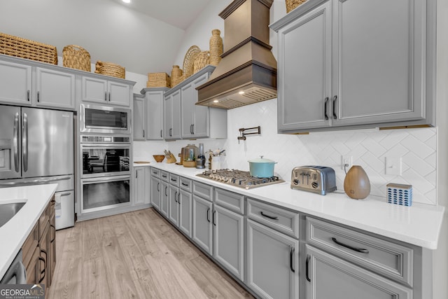 kitchen featuring stainless steel appliances, light countertops, light wood-style flooring, and custom range hood