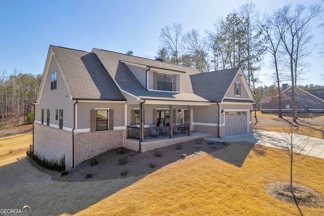 view of front of home featuring concrete driveway, roof with shingles, covered porch, a front lawn, and brick siding