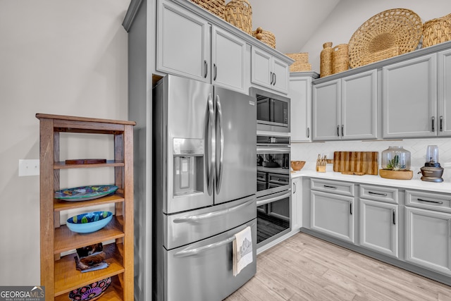 kitchen featuring decorative backsplash, appliances with stainless steel finishes, light countertops, gray cabinetry, and light wood-type flooring