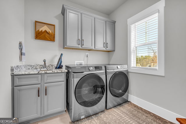 washroom featuring cabinet space, baseboards, a sink, and washing machine and clothes dryer