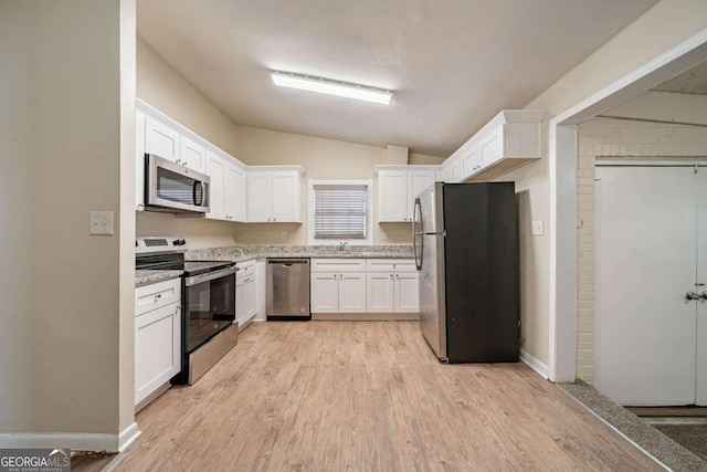 kitchen with white cabinets, lofted ceiling, stainless steel appliances, light wood-style floors, and a sink