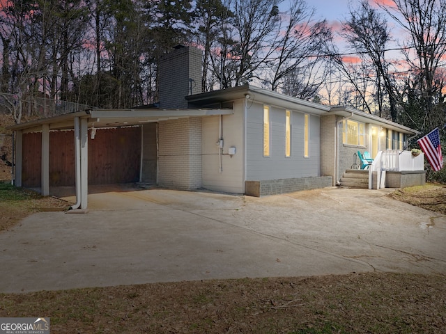 view of side of property featuring a carport, concrete driveway, brick siding, and a chimney