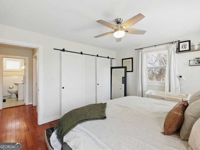 bedroom featuring a barn door, dark wood finished floors, a ceiling fan, and baseboards