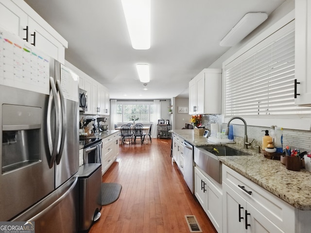 kitchen featuring visible vents, light stone countertops, stainless steel appliances, white cabinetry, and backsplash