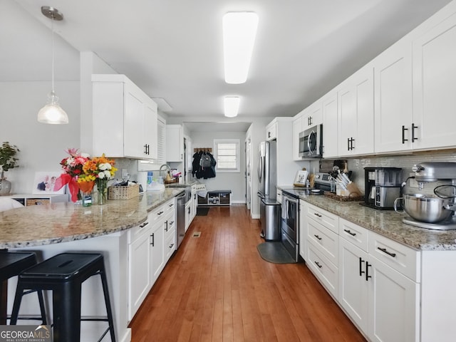 kitchen featuring a peninsula, white cabinetry, stainless steel appliances, and decorative light fixtures