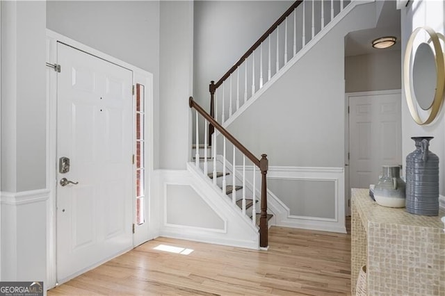 foyer with light wood-style floors, wainscoting, a decorative wall, and stairway