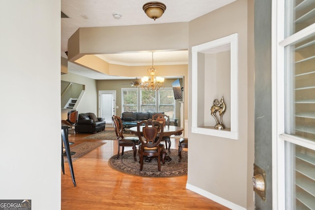 dining space with a chandelier, wood finished floors, baseboards, stairway, and crown molding