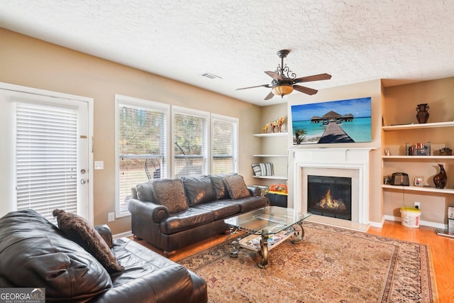 living area featuring a textured ceiling, a fireplace with flush hearth, wood finished floors, visible vents, and built in features