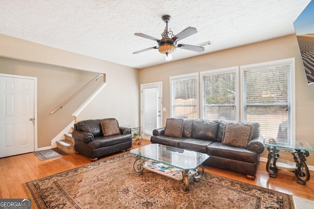 living area featuring stairway, ceiling fan, a textured ceiling, wood finished floors, and baseboards