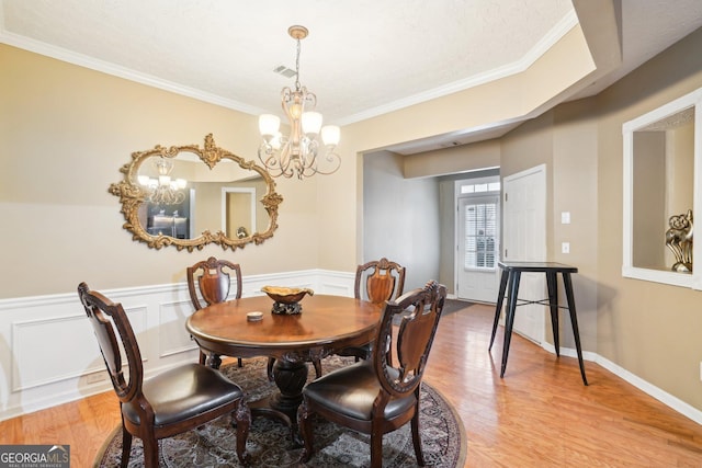 dining room featuring light wood-type flooring, wainscoting, visible vents, and an inviting chandelier