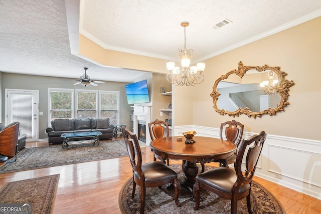 dining space with a wainscoted wall, wood finished floors, a glass covered fireplace, and visible vents