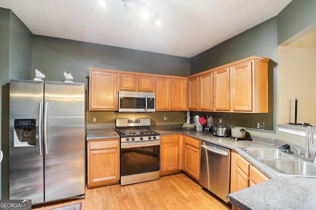 kitchen with stainless steel appliances, a sink, light wood-style flooring, and a textured ceiling