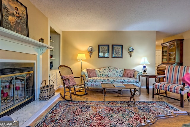 living room featuring a textured ceiling, baseboards, a glass covered fireplace, and light wood-style floors