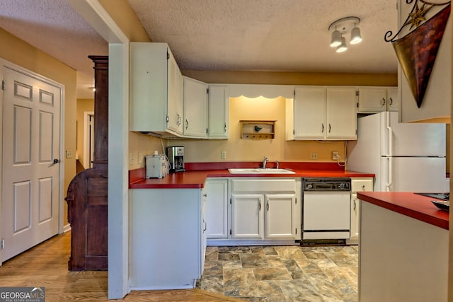 kitchen featuring dark countertops, white cabinets, a sink, a textured ceiling, and white appliances