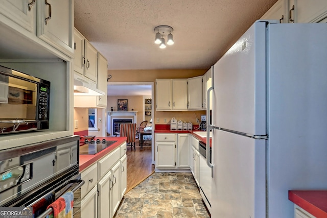 kitchen featuring stone finish floor, white cabinetry, under cabinet range hood, and black appliances