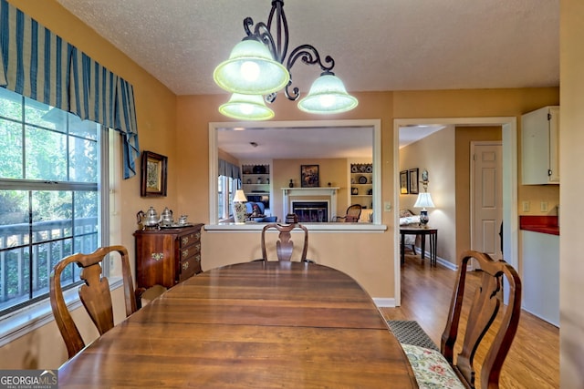 dining room with light wood-style floors, a textured ceiling, and a glass covered fireplace