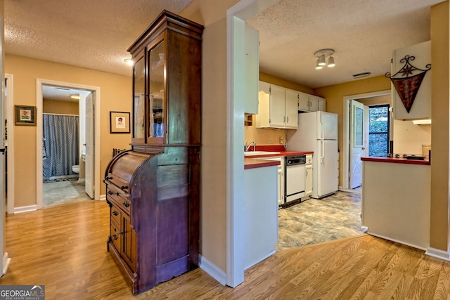 kitchen featuring white appliances, light wood-style flooring, glass insert cabinets, a textured ceiling, and white cabinetry