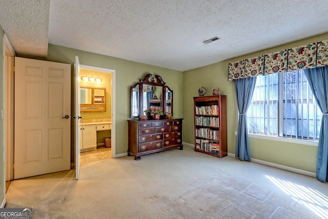 bedroom with light carpet, baseboards, visible vents, ensuite bath, and a textured ceiling