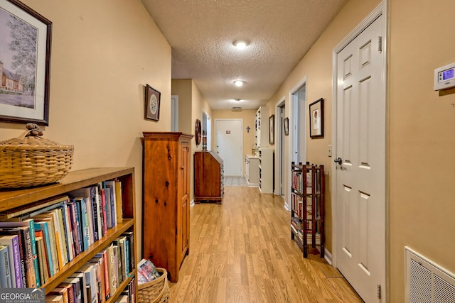 hall with light wood-type flooring, visible vents, and a textured ceiling