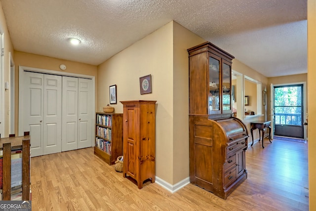 hall featuring a textured ceiling, light wood-type flooring, and baseboards