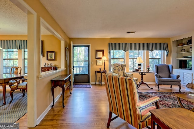 sitting room featuring visible vents, a textured ceiling, baseboards, and wood finished floors