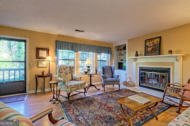 living room with light wood-type flooring, baseboards, visible vents, and a textured ceiling