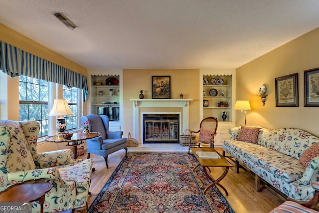 living room featuring light wood-type flooring, built in shelves, visible vents, and a glass covered fireplace