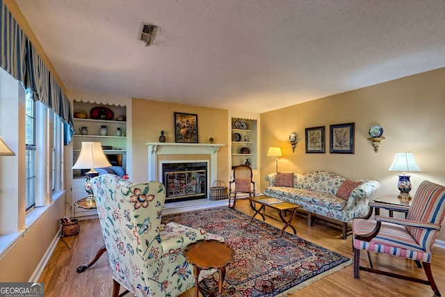 living room featuring visible vents, a glass covered fireplace, wood finished floors, a textured ceiling, and built in shelves