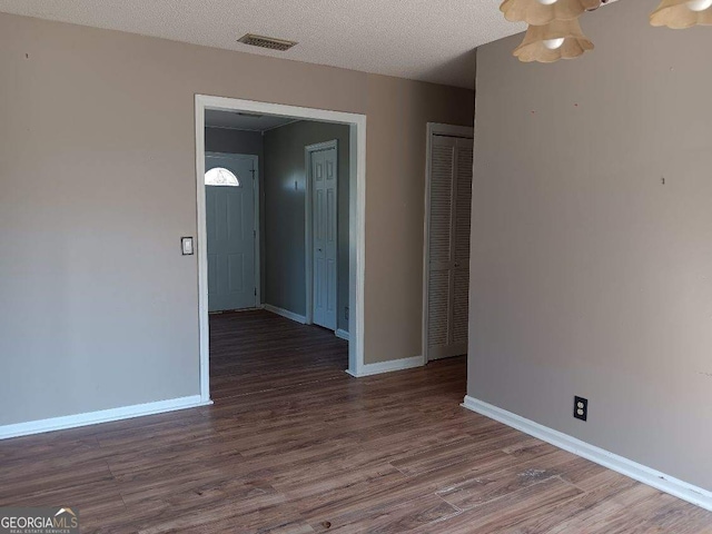 empty room featuring visible vents, a textured ceiling, baseboards, and wood finished floors