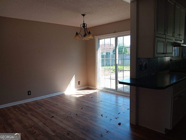 unfurnished dining area with a textured ceiling, a chandelier, wood finished floors, and baseboards