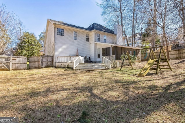 rear view of property with a playground, fence, a sunroom, a lawn, and a chimney