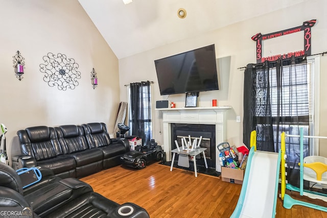 living room featuring plenty of natural light, high vaulted ceiling, wood finished floors, and a glass covered fireplace