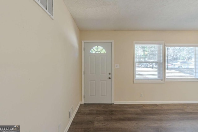 foyer entrance with dark wood-type flooring, visible vents, a textured ceiling, and baseboards