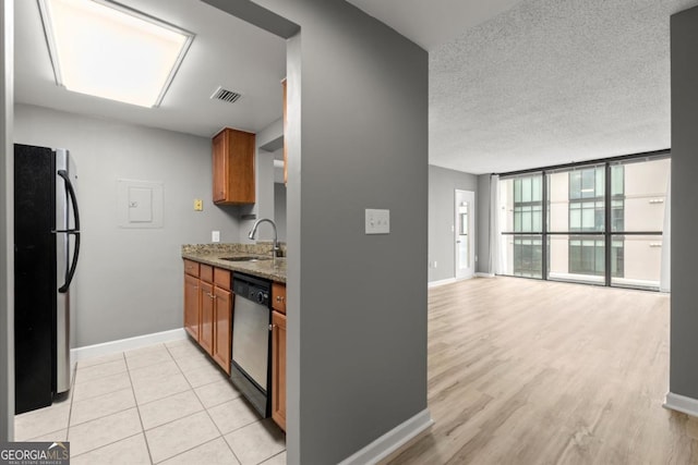 kitchen with stainless steel appliances, a sink, visible vents, light stone countertops, and brown cabinetry