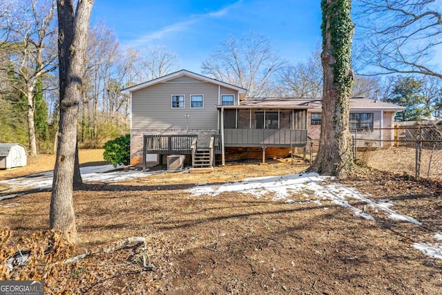 back of house featuring a sunroom, fence, a wooden deck, and a storage unit