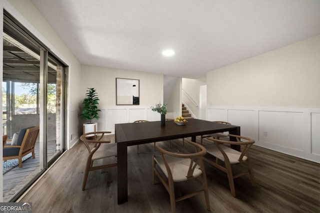 dining room with a wainscoted wall, stairway, dark wood-style flooring, and a decorative wall