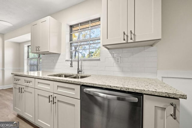 kitchen featuring light stone counters, backsplash, stainless steel dishwasher, white cabinets, and a sink