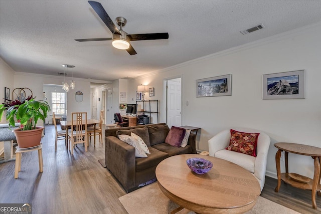 living room featuring ornamental molding, visible vents, light wood-style flooring, and a textured ceiling